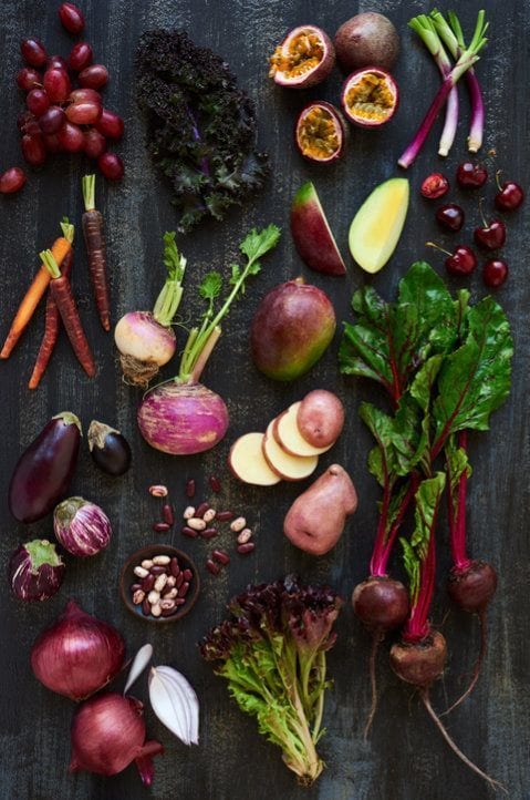 Purple coloured raw fruits and veggies on dark background